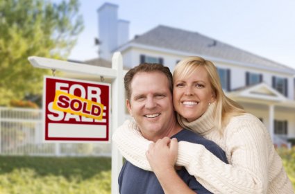 33420961 - affectionate happy couple in front of new house and sold for sale real estate sign.