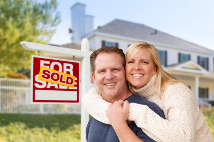 33420961 - affectionate happy couple in front of new house and sold for sale real estate sign.