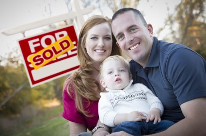 Happy Young Caucasian Family in Front of Sold Real Estate Sign.